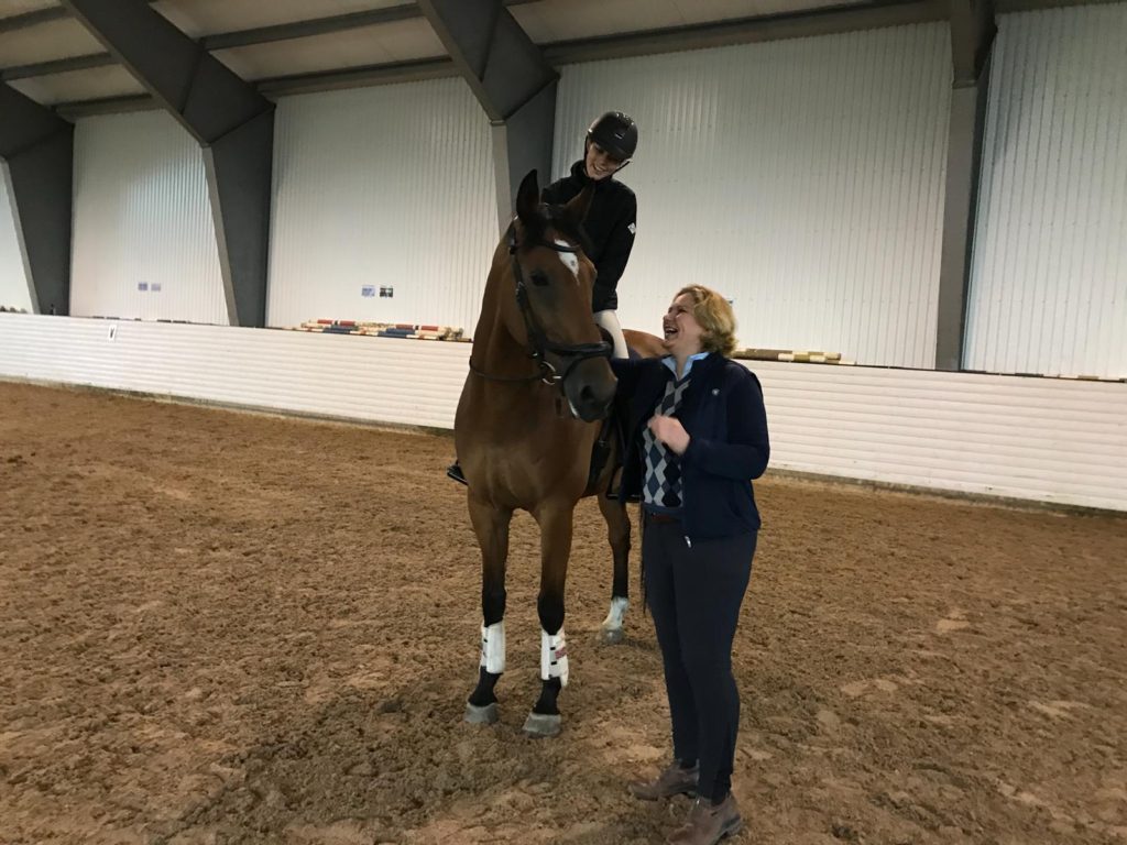 Kvinne på brun hest med trener in i ridehuset
